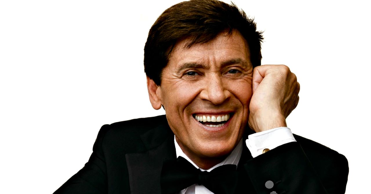 Gianni Morandi sorride con mano sul viso