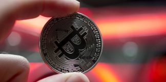 Una moneta dei BTC sorretta da una mano davanti a delle luci